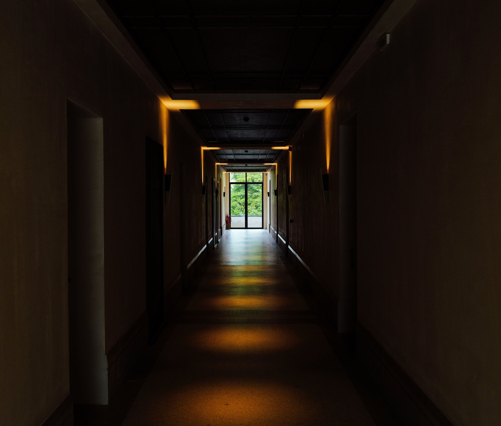 Dark corridor with warm lights leading to a lit doorway